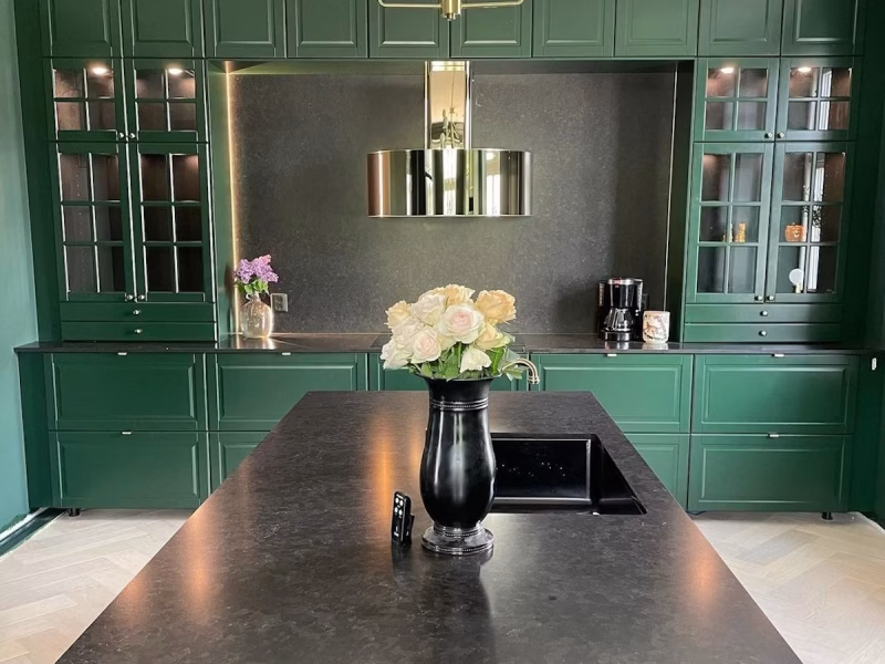 Green shaker kitchen with a dark stone island and integrated sink