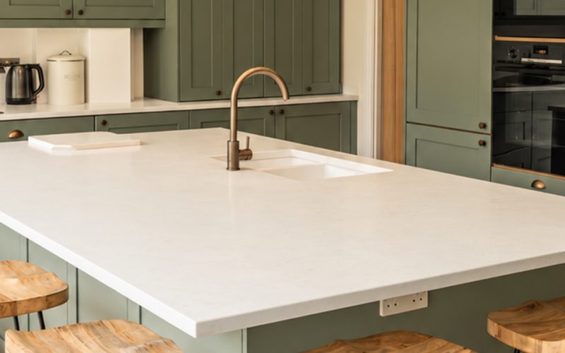 Sage green kitchen cabinets with Bianco Carrara worktops and a large white kitchen island